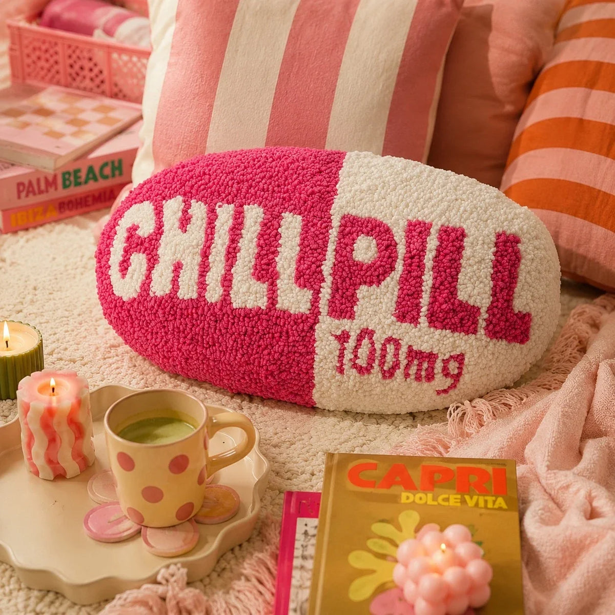 Chill Pill pillow on a striped pink bed with a candle and a matcha mug