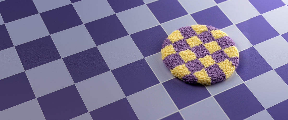 A purple and yellow checkerboard punch needle mug rug on a purple checked floor