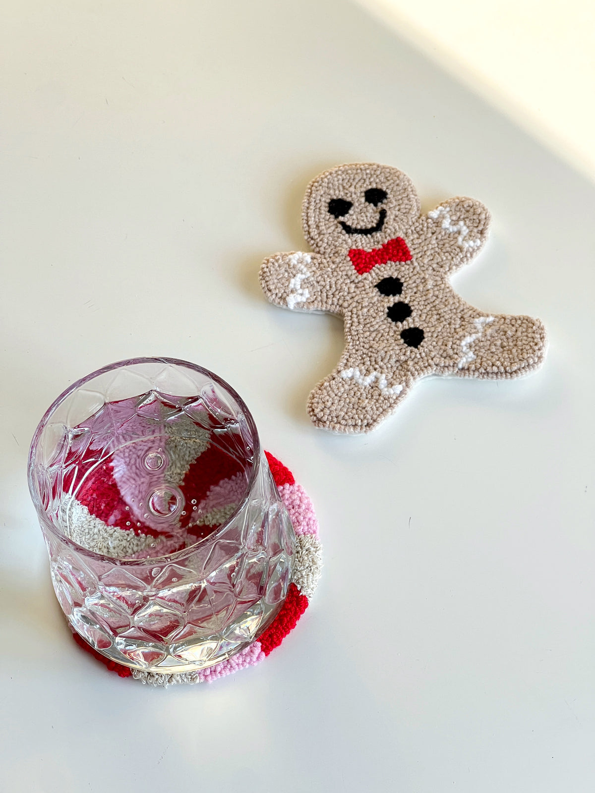 Gingerbread man punch needle coaster beside a glass resting on a peppermint coaster