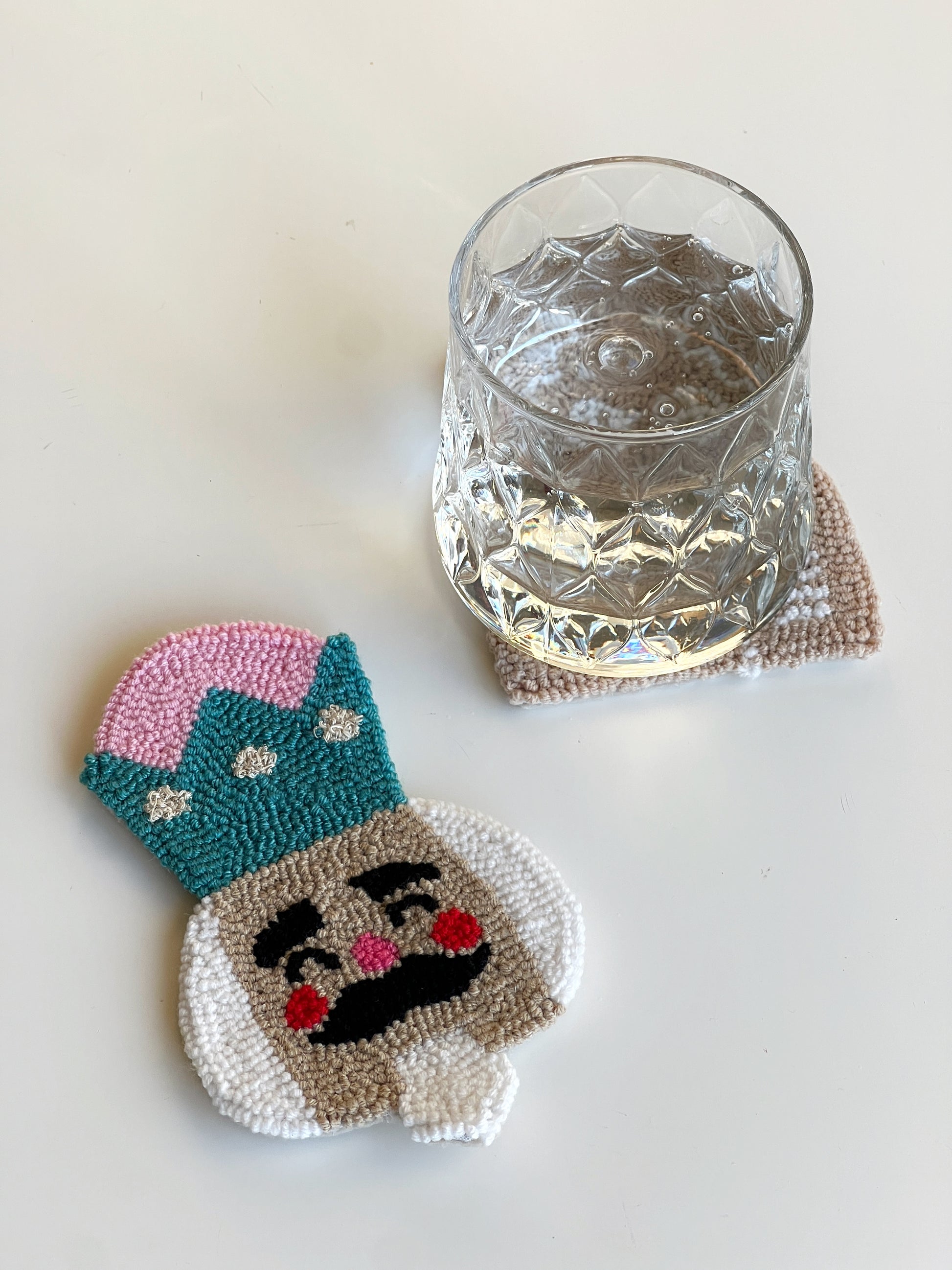 Nutcracker punch needle coaster beside a cut glass of water
