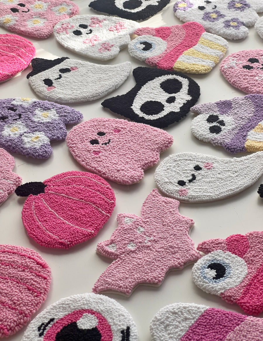 Flat lay of pastel pink Halloween punch needle coasters with ghosts, bats and candy corn