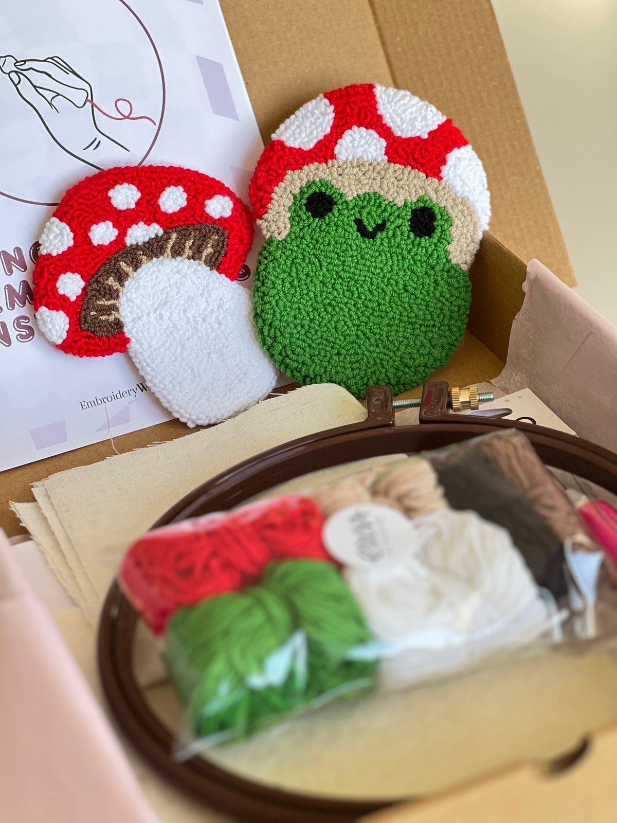 Punch needle kit box with frog and mushroom coasters, yarn, hoop and needle