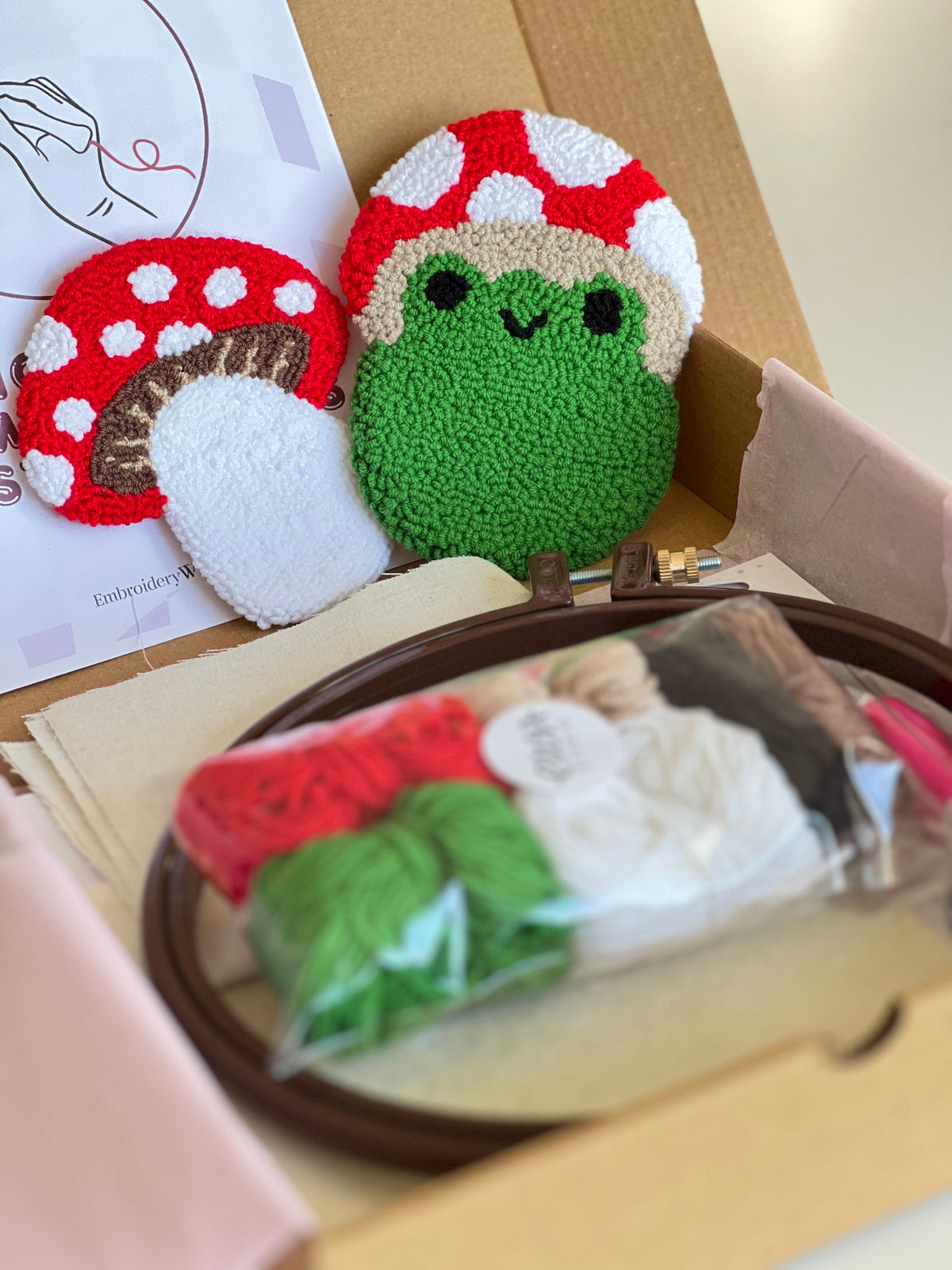 Punch needle kit box with frog and mushroom coasters, yarn, hoop and needle