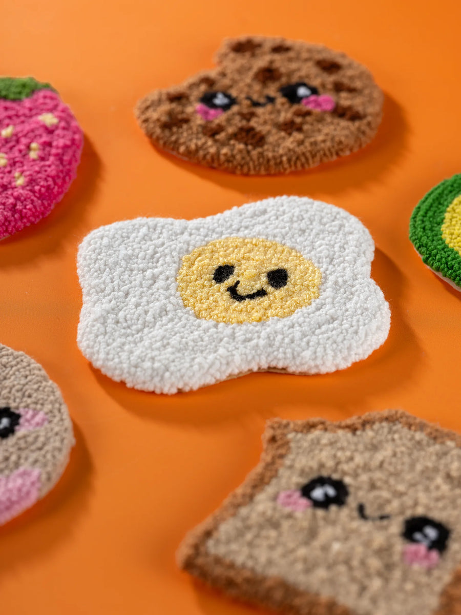 Kawaii punch needle mug rugs on an orange still-life set
