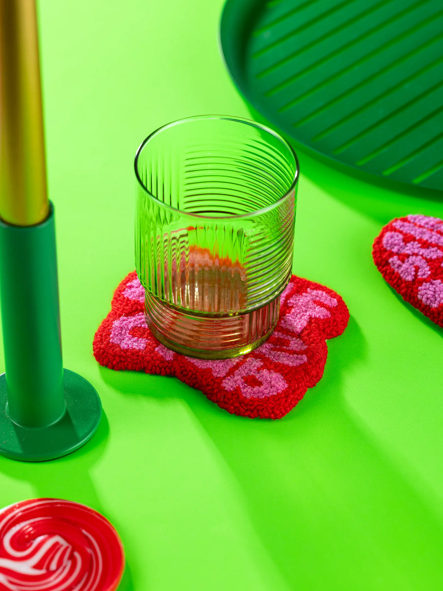 Punch needle coaster in use under a ribbed glass on a lime green set